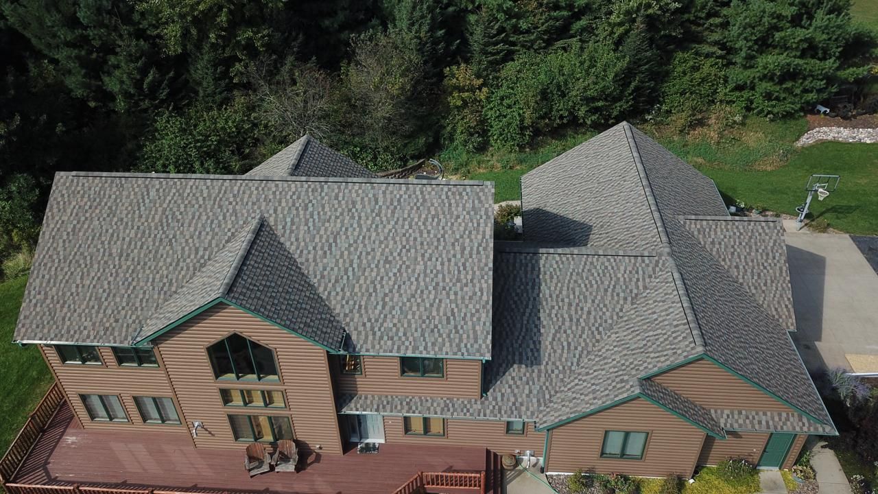 An aerial view of a large house with a gray roof surrounded by trees.