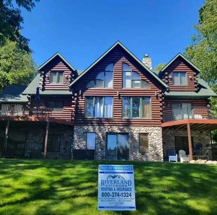 A large log cabin with a riverland roofing and insurance sign in front of it — Holmen, WI — Riverland Exteriors Corporation