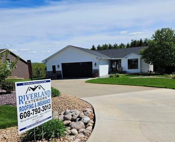 A sign for riverland exterior roofing and insurance is in front of a house — Holmen, WI — Riverland Exteriors Corporation