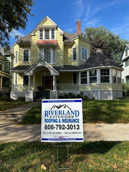 A yellow house with a riverland roofing and insurance sign in front of it — Holmen, WI — Riverland Exteriors Corporation