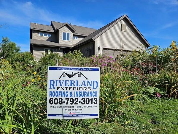 A sign for riverland exteriors roofing and insurance is in front of a house — Holmen, WI — Riverland Exteriors Corporation