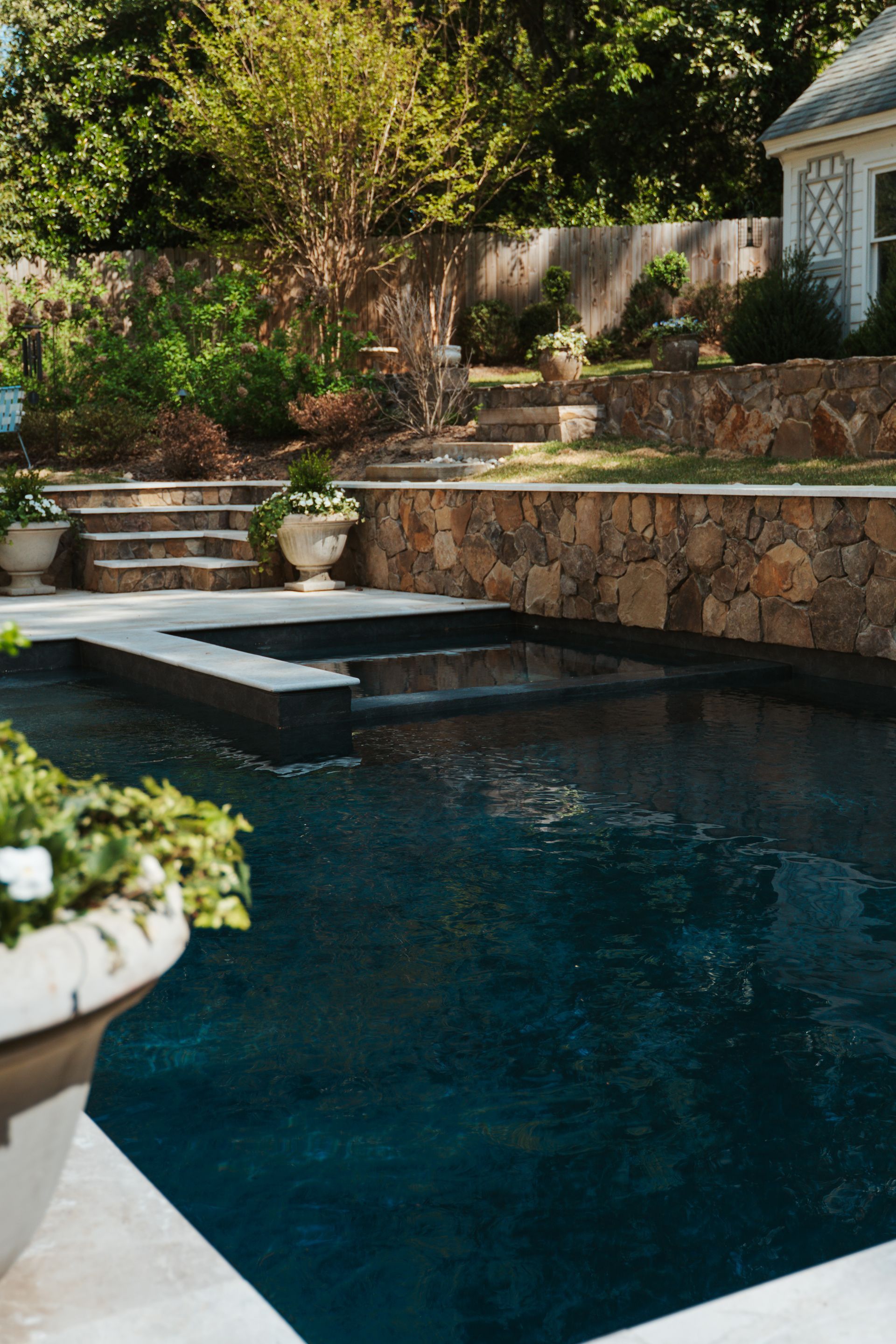 Backyard pool with dark blue water, stone steps, and a landscaped patio beside a house