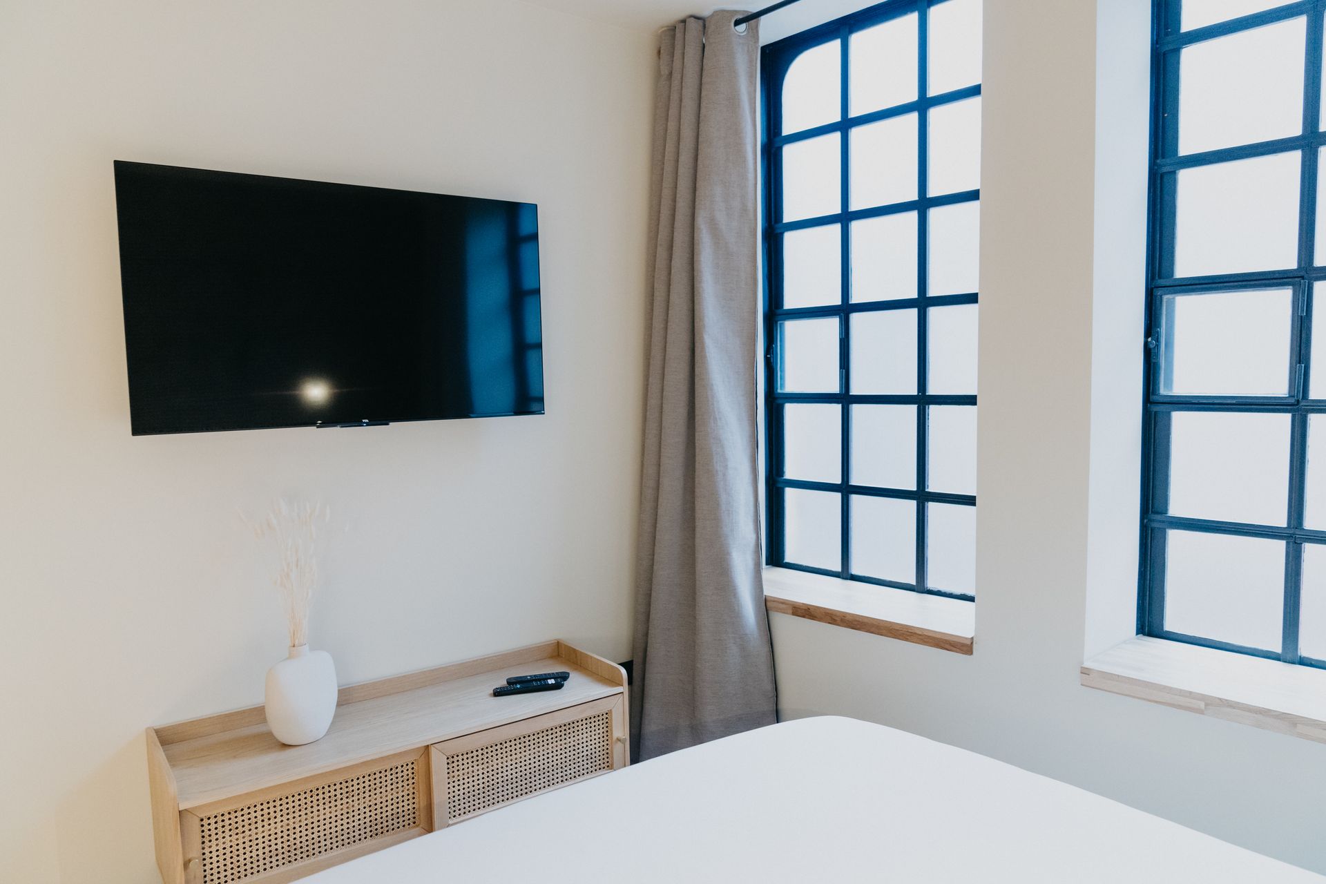 Une chambre avec un lit, une télévision et deux fenêtres.