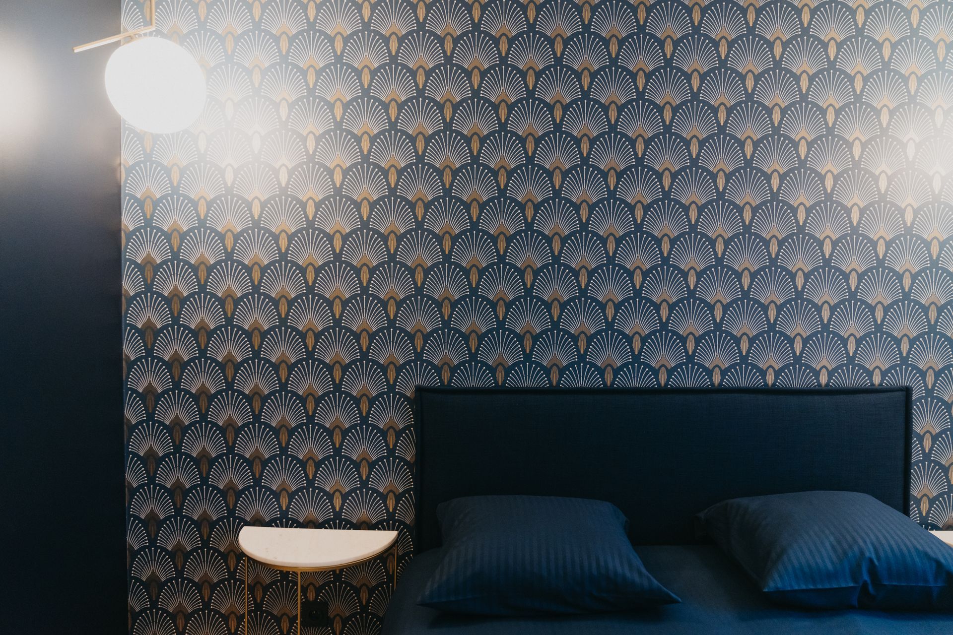 Une chambre avec un lit, une table de nuit, une lampe et du papier peint.