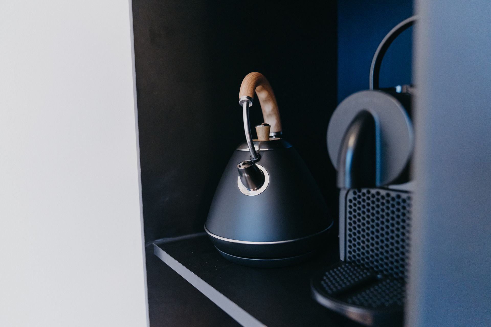 Une bouilloire à thé noire est posée sur une étagère dans une pièce sombre.