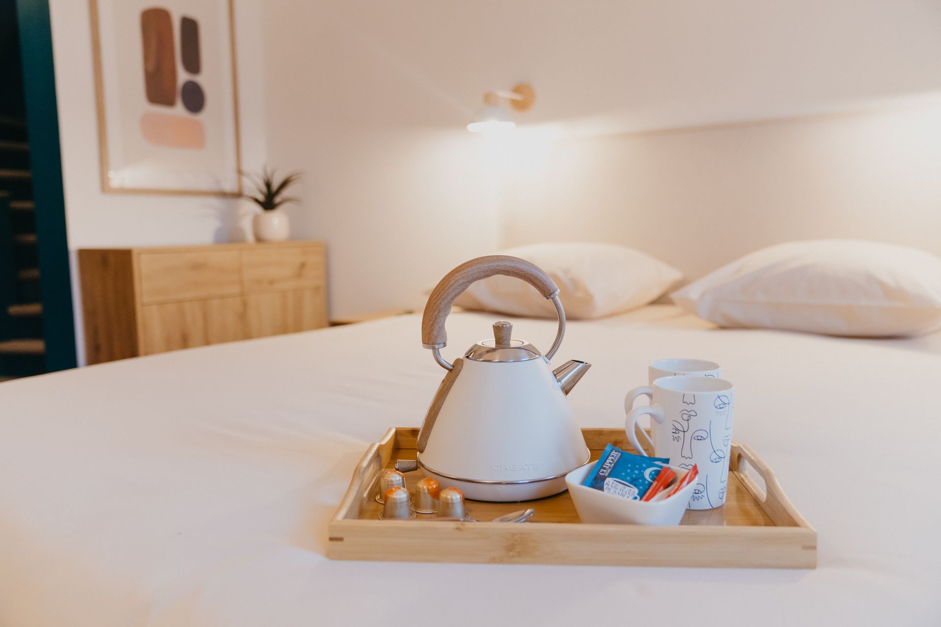 Un plateau en bois avec une bouilloire, des tasses et du sucre sur un lit.