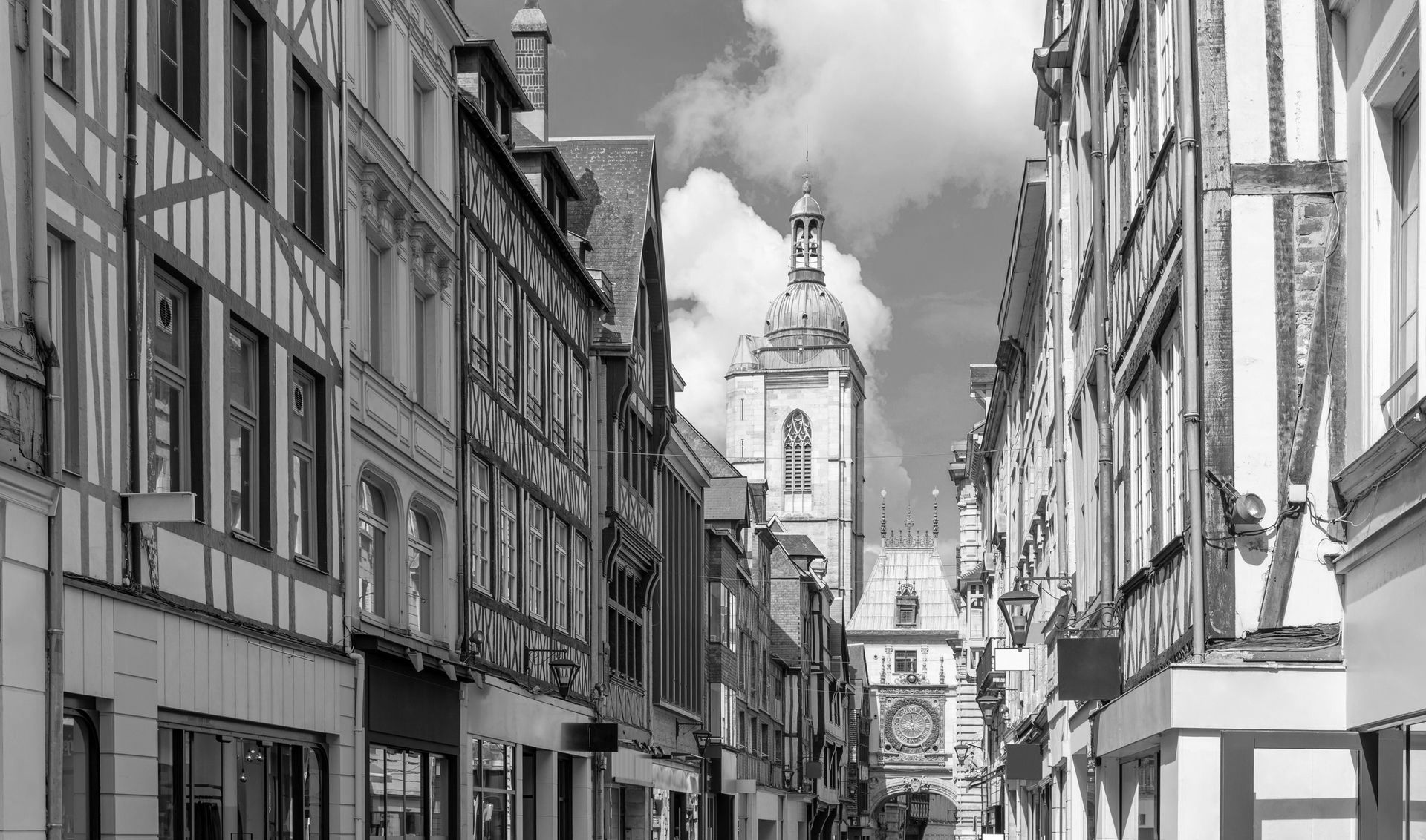 Une photo en noir et blanc d'une rue de la ville avec une tour de l'horloge en arrière-plan.