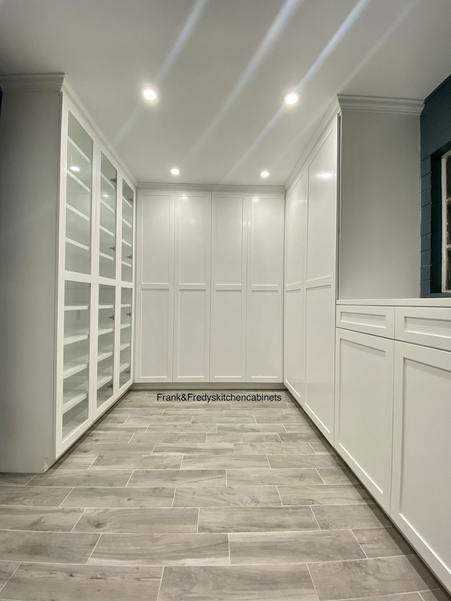 A large walk in closet with white cabinets and glass doors.