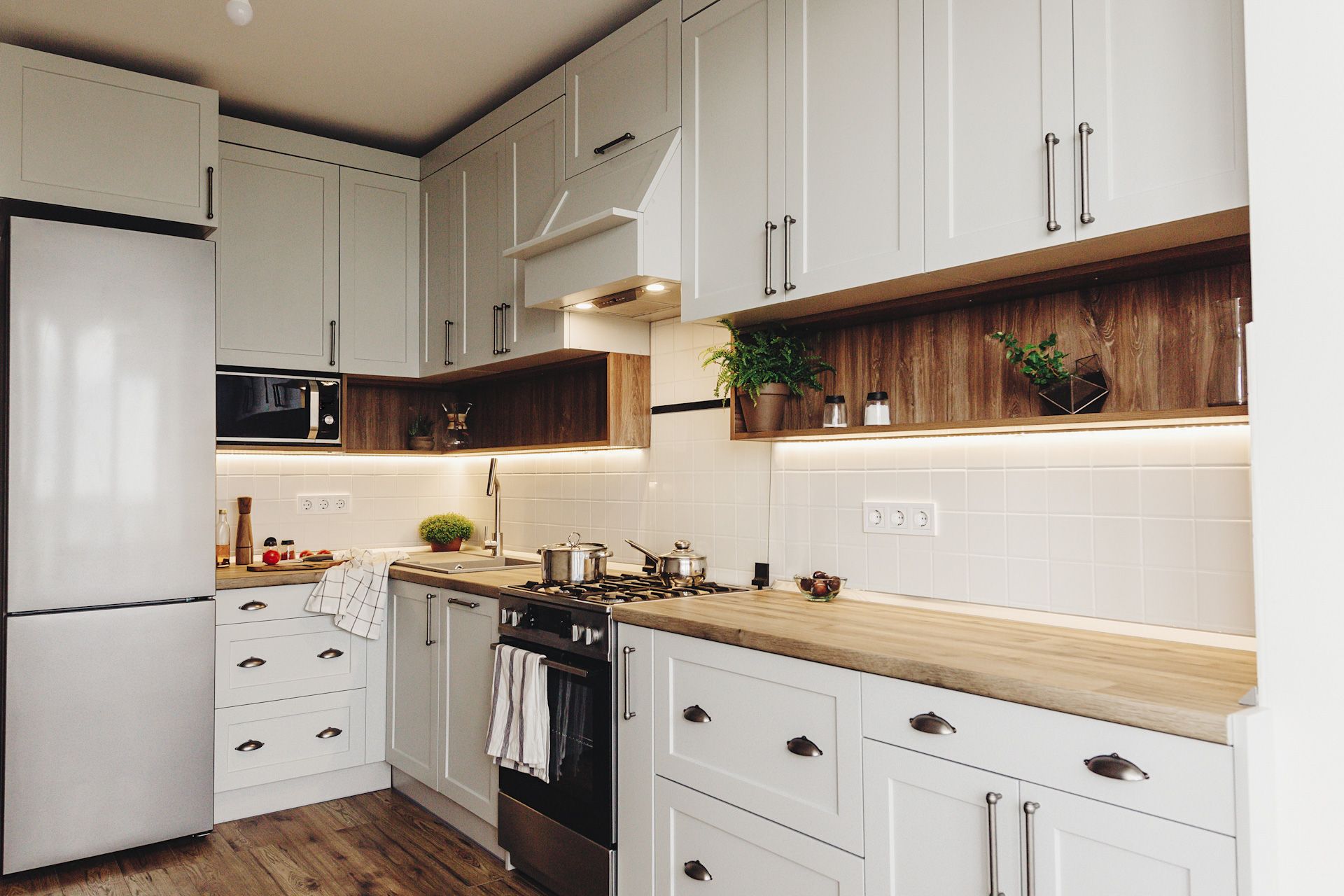 A kitchen with white cabinets , wooden counter tops , stainless steel appliances and a refrigerator.