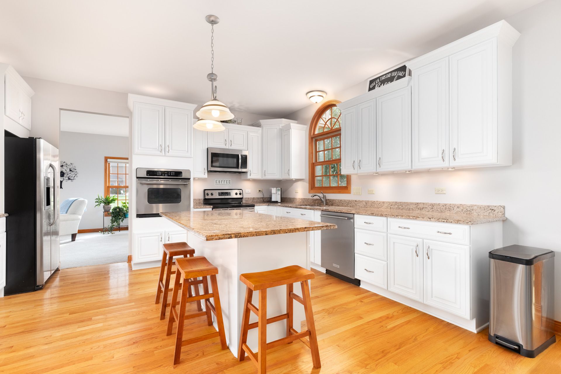 A kitchen with white cabinets, granite counter tops, stools and a trash can.