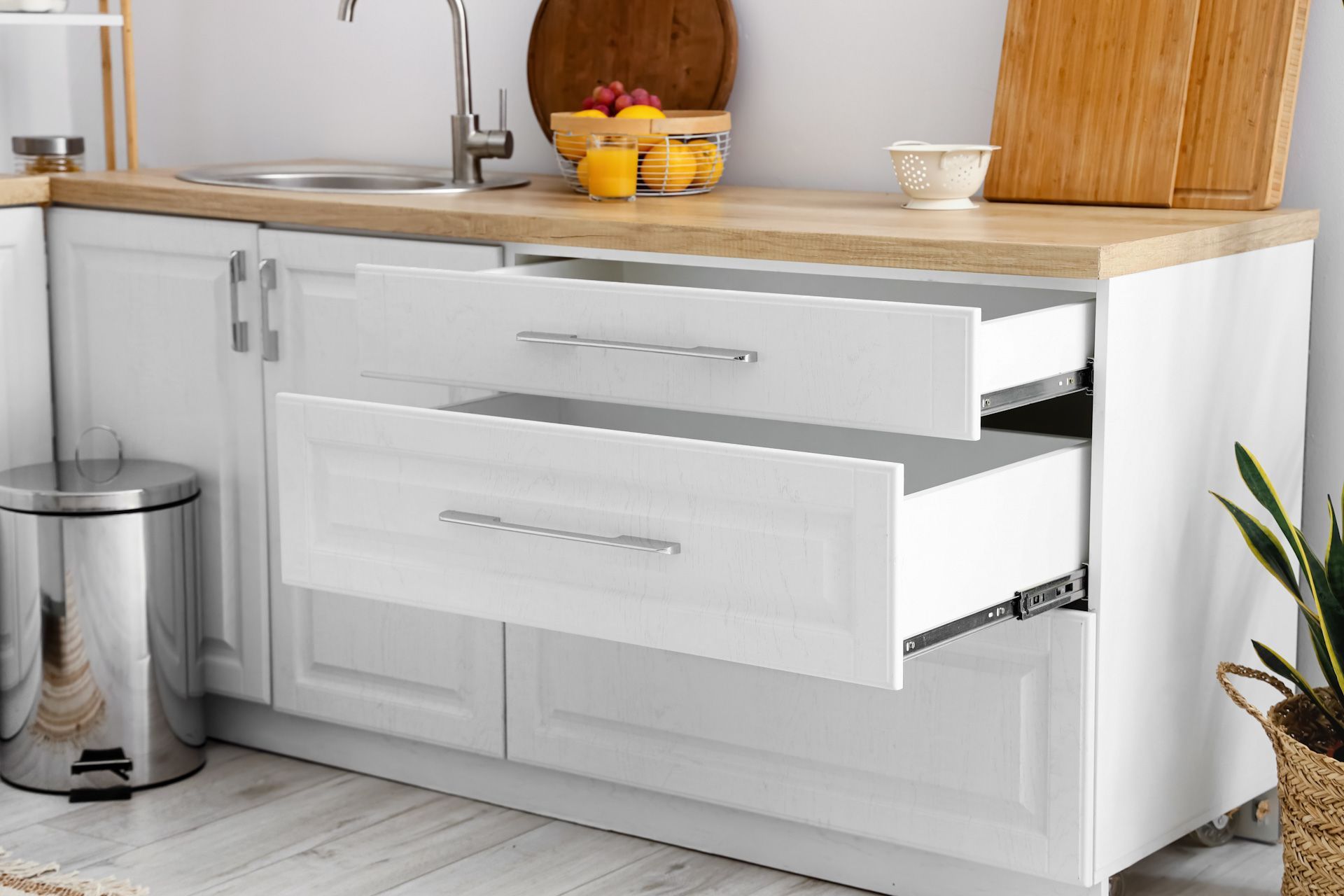 A kitchen with white cabinets, a sink, a trash can, and an open drawer.
