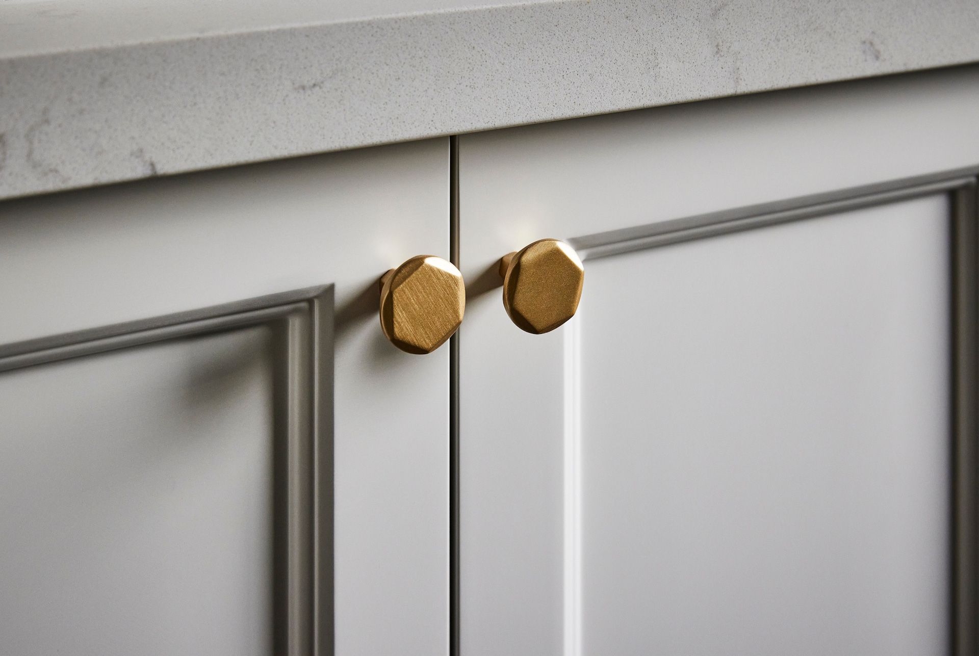 A close up of a cabinet with brass handles and a marble counter top.