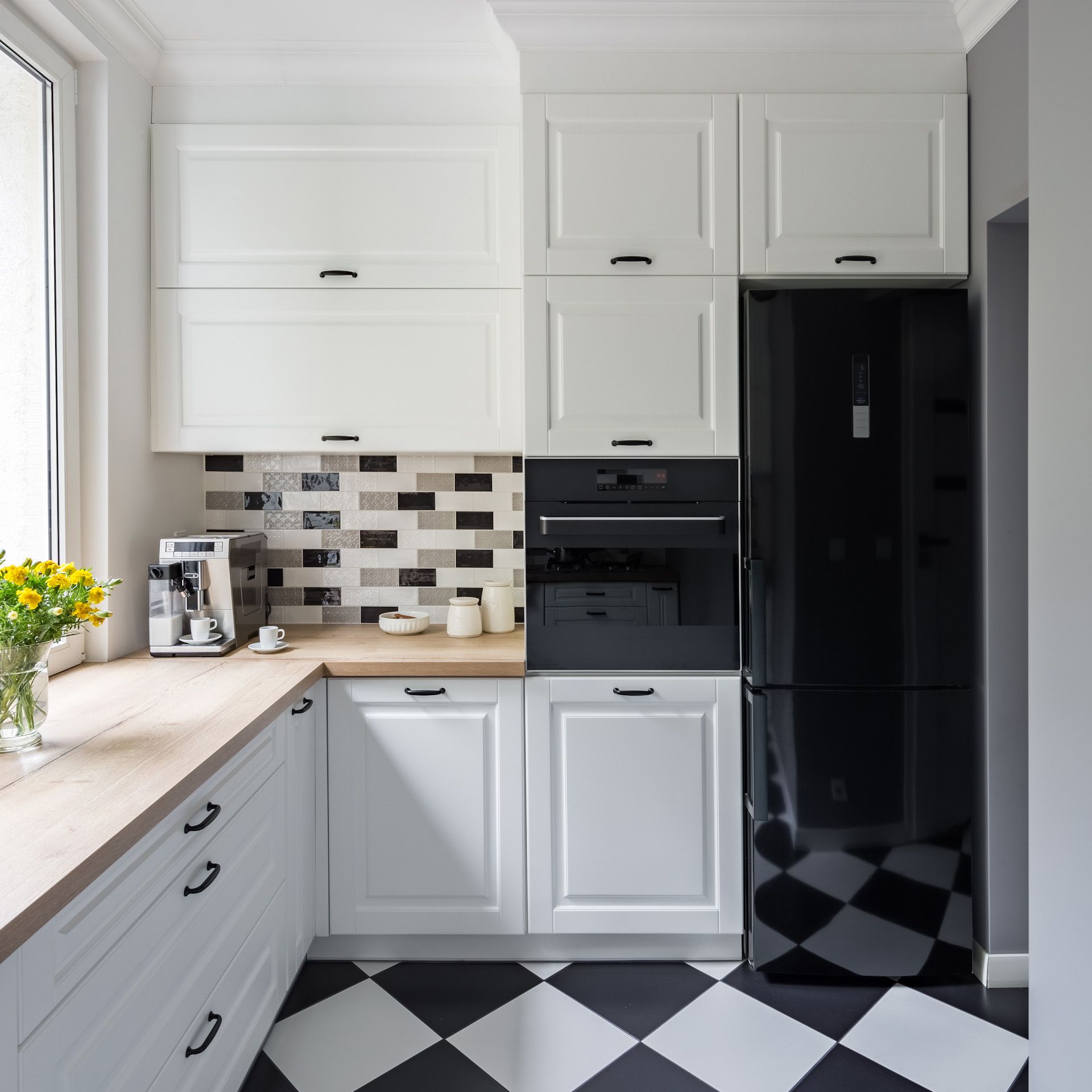 A kitchen with white cabinets black appliances and a checkered floor