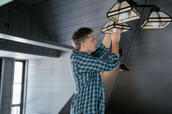 A man in a plaid shirt is hanging a light fixture from the ceiling.