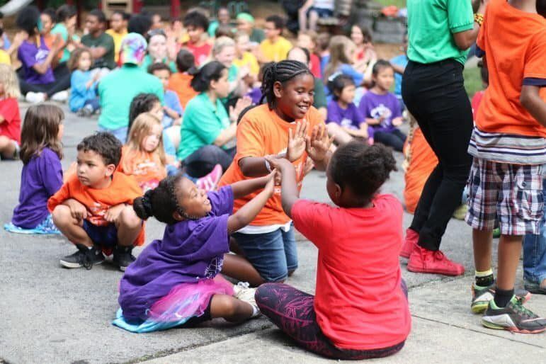 A group of children are sitting on the ground playing with each other.