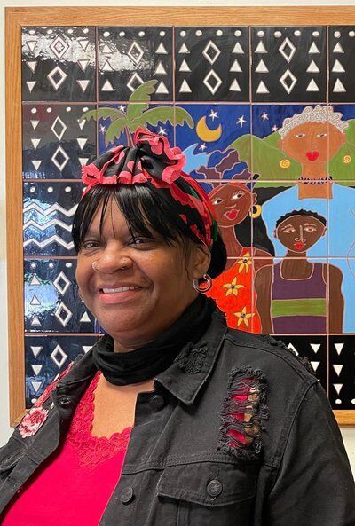 A woman wearing a red headband and a black jacket is smiling in front of a painting.