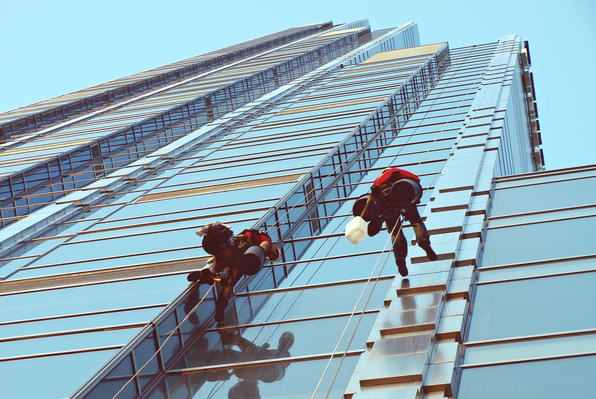 Window cleaner hanging on a skyscraper, cleaning a glass facade, reflected sky and buildings.