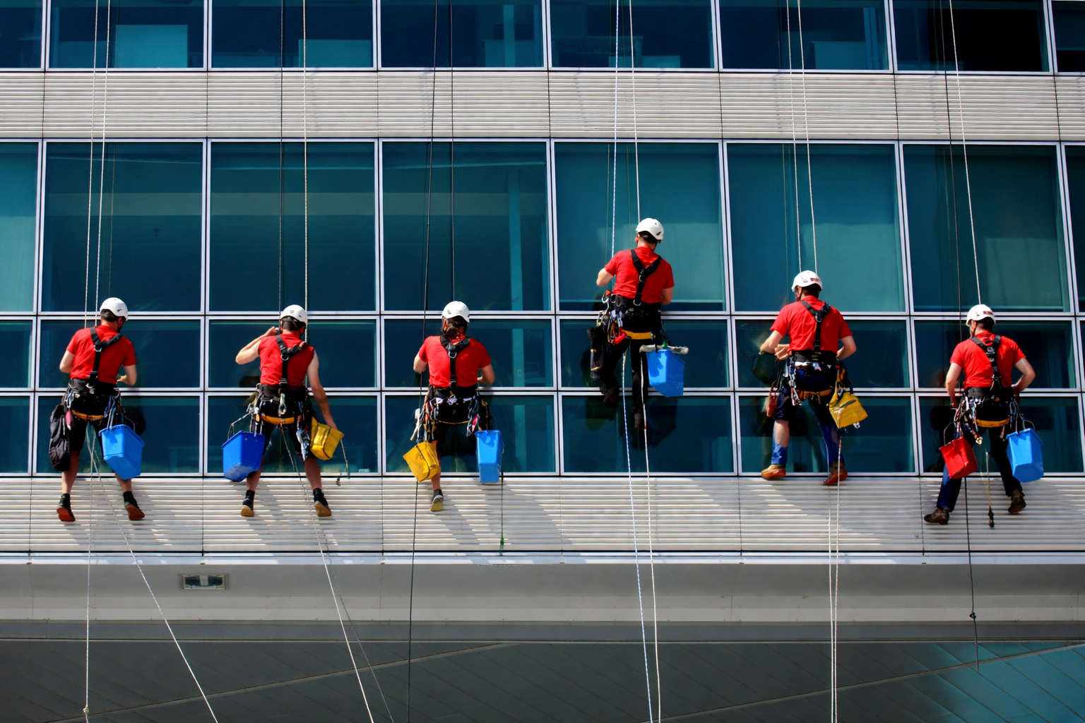Window cleaner hanging on a skyscraper, cleaning a glass facade, reflected sky and buildings.