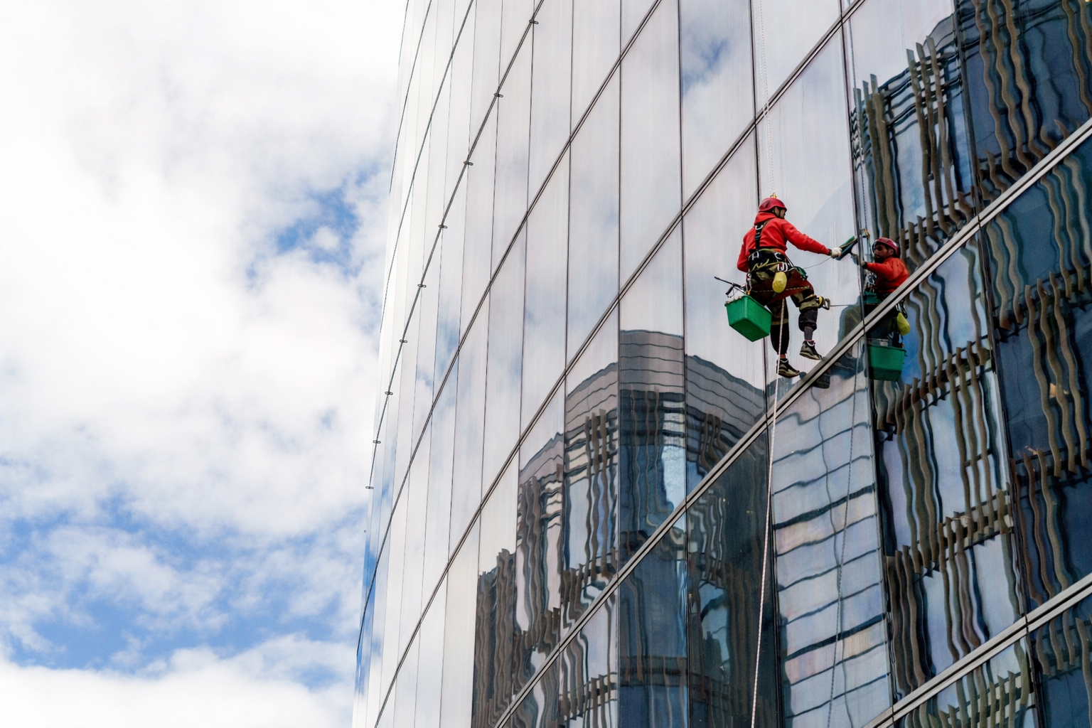 Window cleaner hanging on a skyscraper, cleaning a glass facade, reflected sky and buildings.