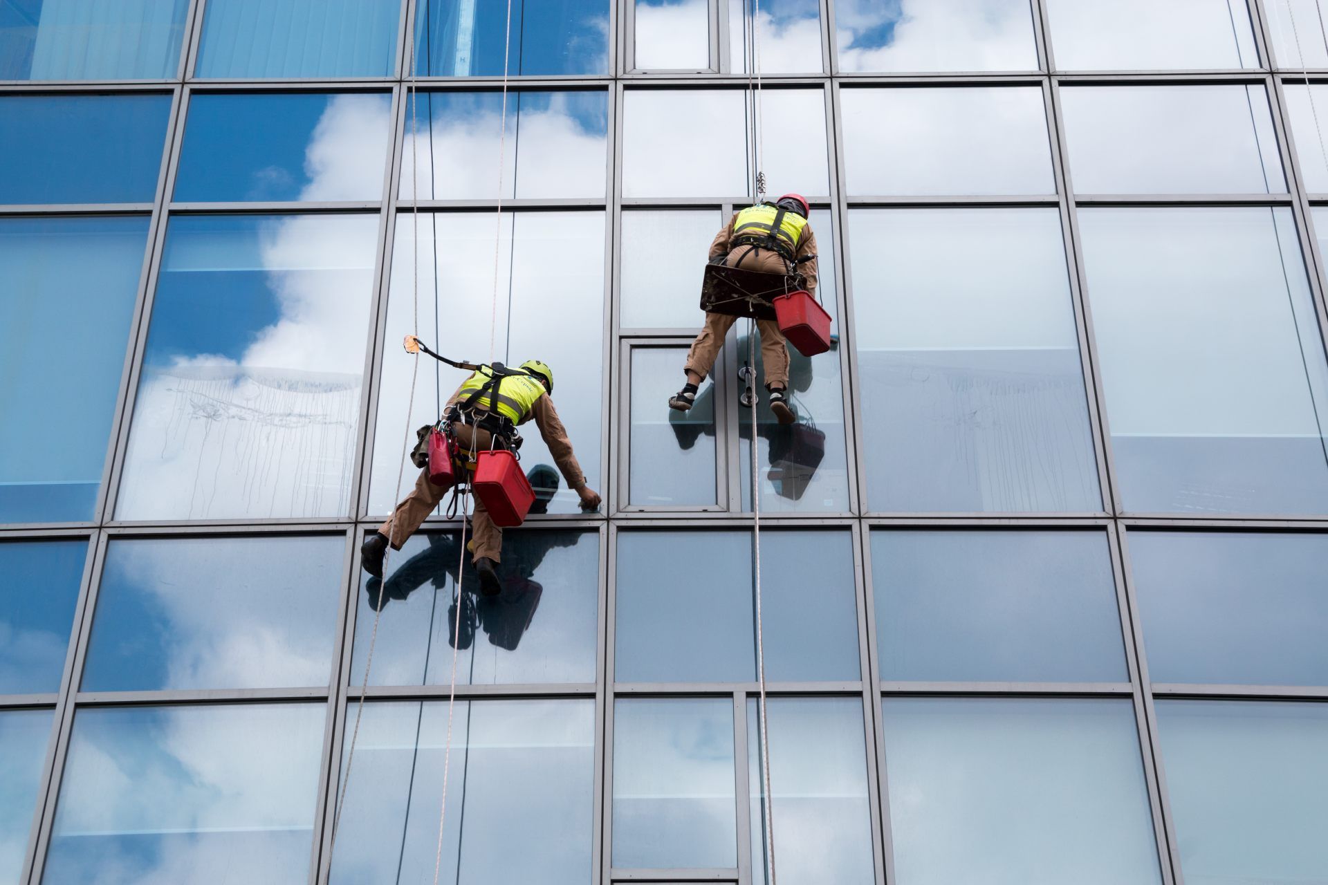 A window washer in a harness sprays water on a tall building, blue glass and white walls.