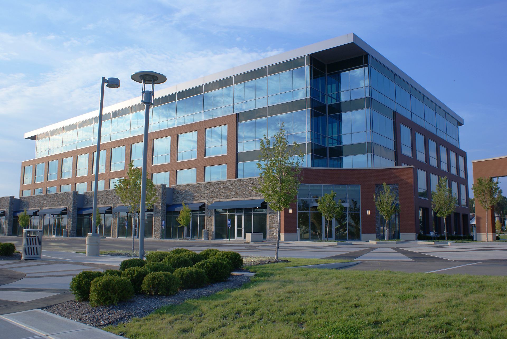 A modern four-story office building with brick, glass, and stone exterior, surrounded by parking and landscaping.