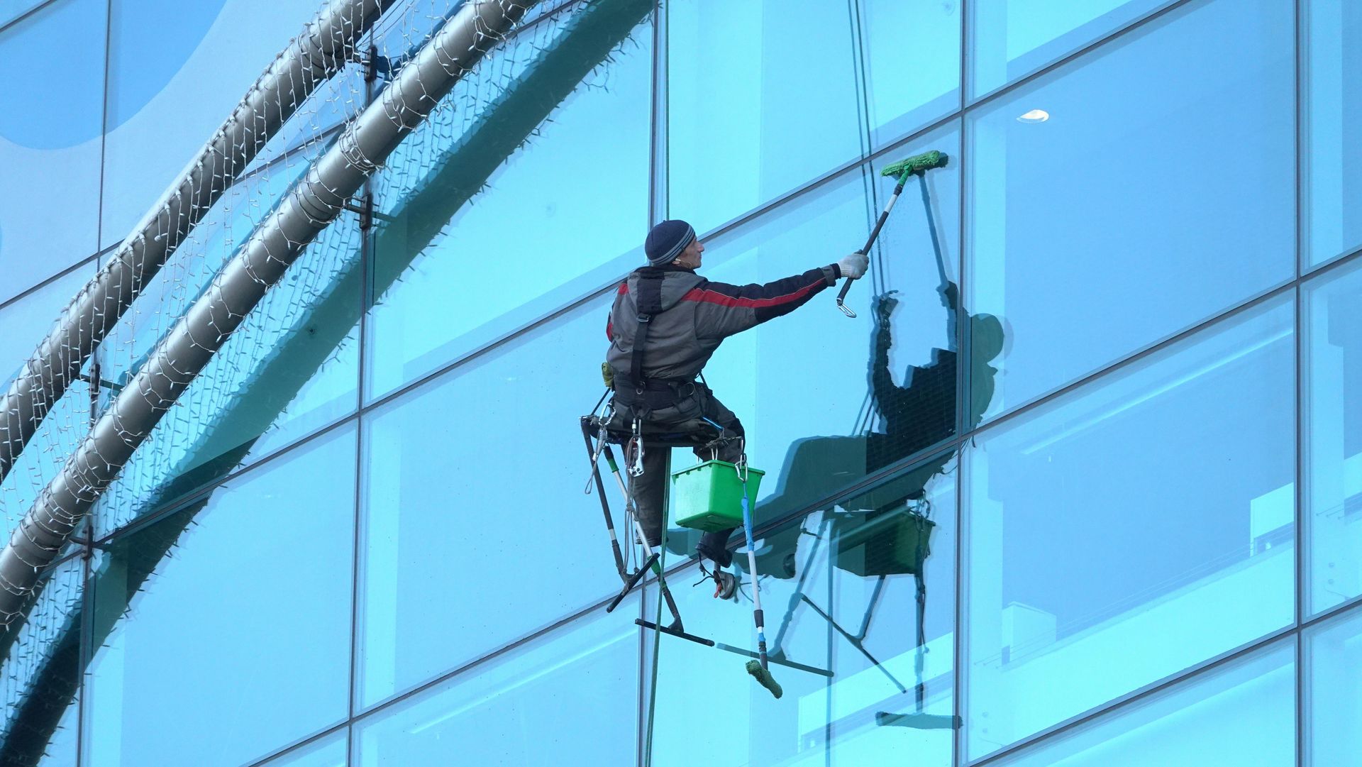 Window washer on a suspended platform cleaning a large glass building; blue sky.