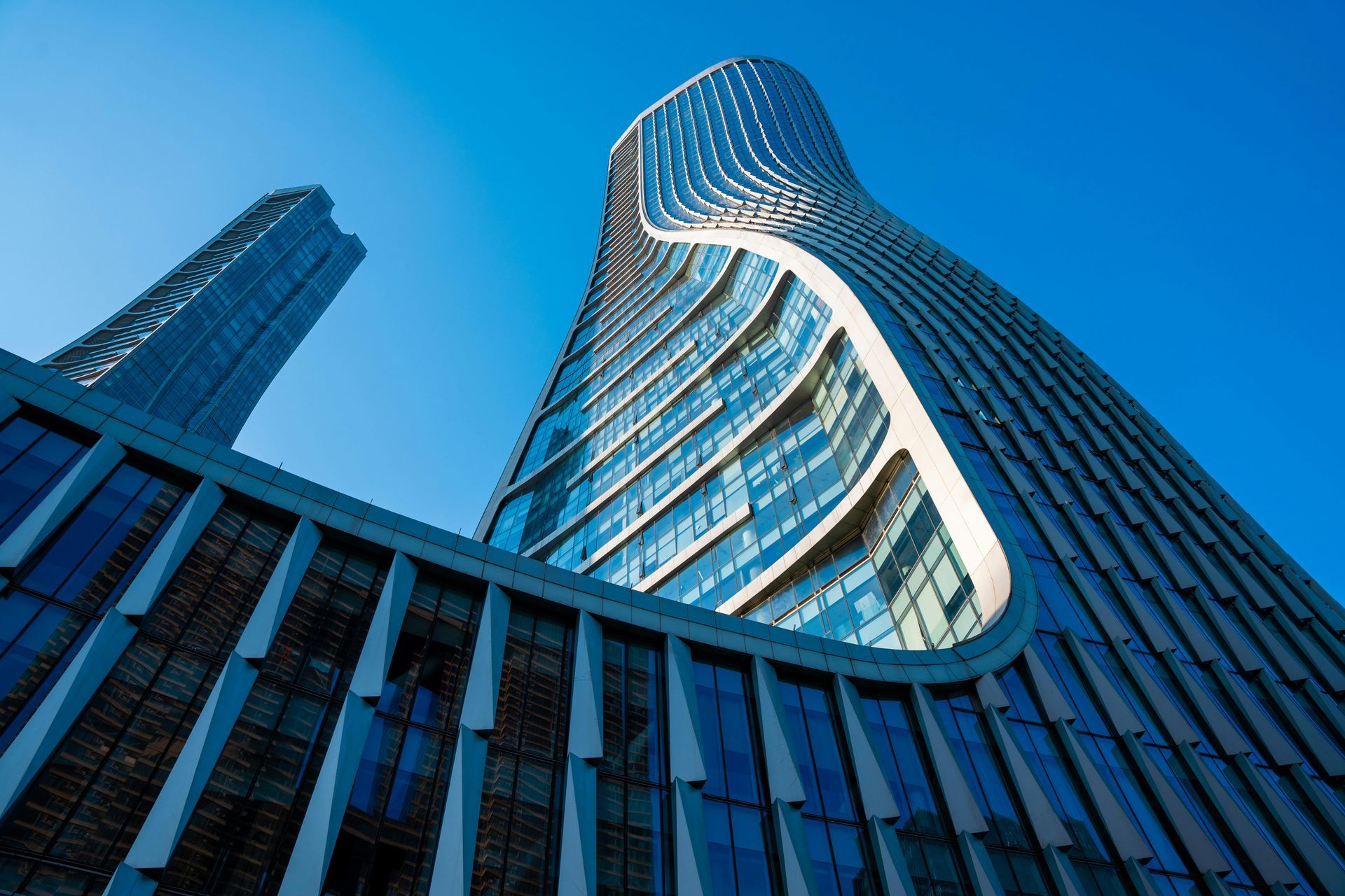 Low-angle view of a modern, curved glass skyscraper reaching toward a bright blue sky.