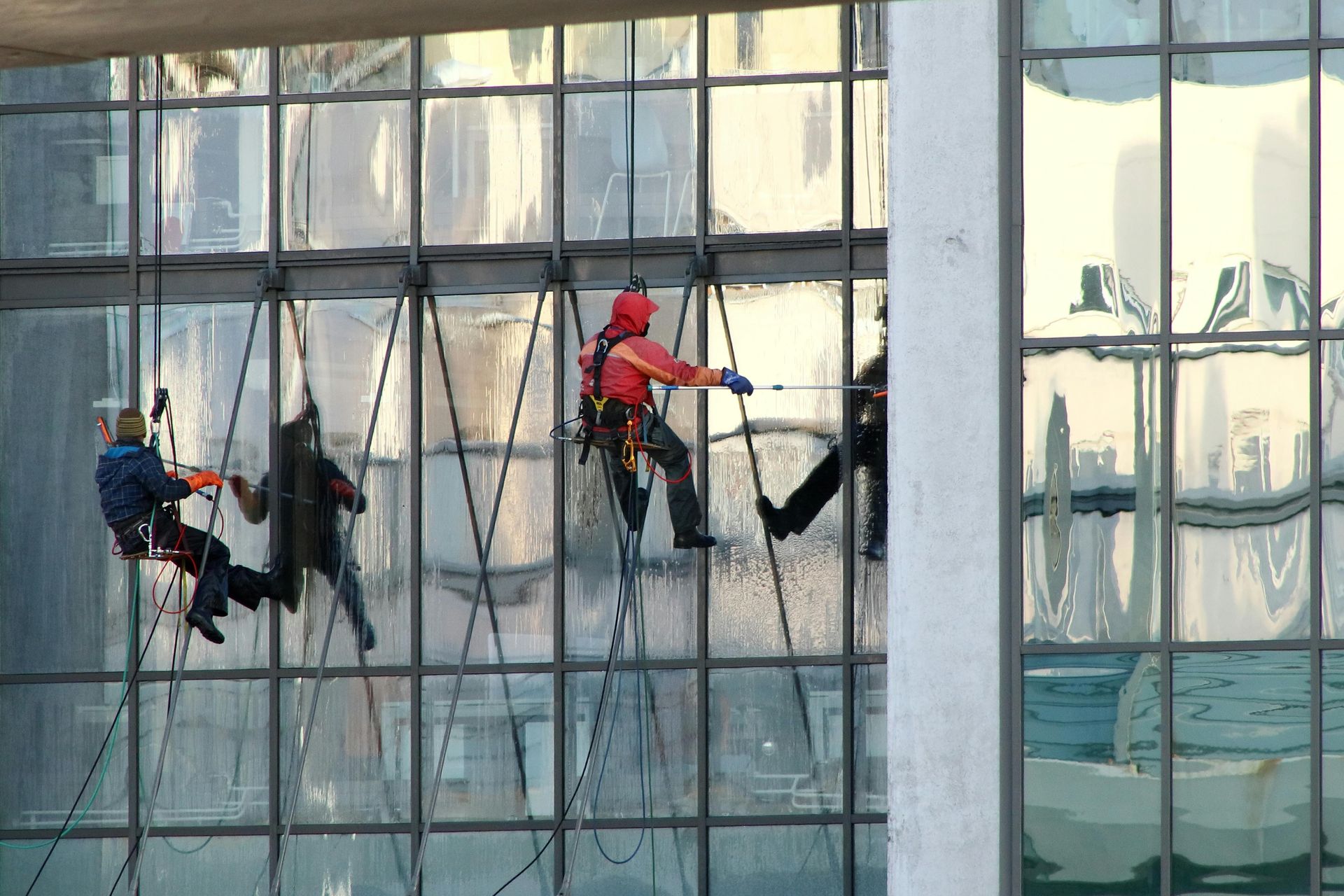 Window washers on ropes cleaning a large glass building's exterior.