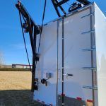 White industrial trailer with black crane arm raised beside it in a field under a blue sky