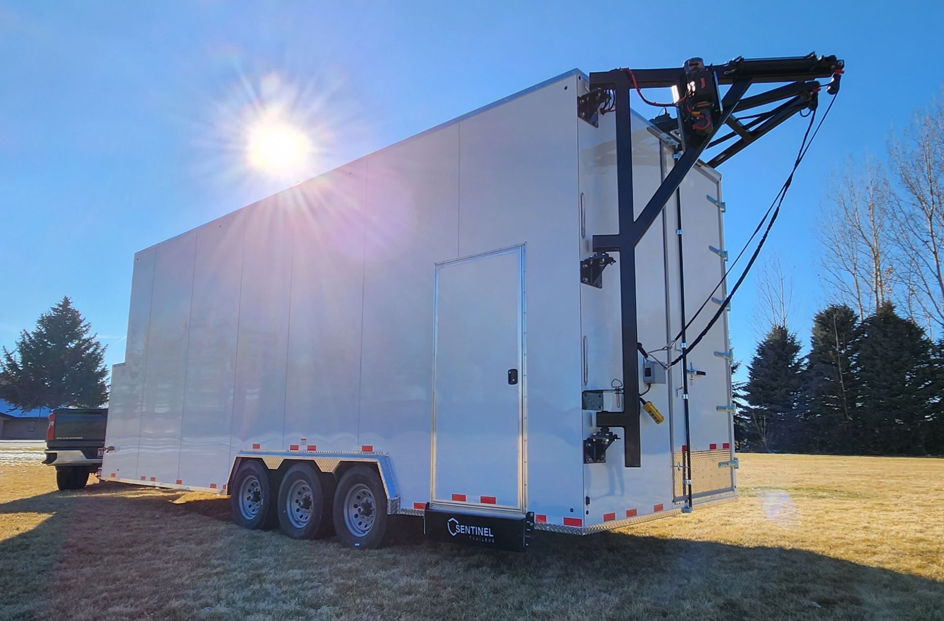 White enclosed slaugther trailer trailer with side door and rear liftgate, parked on grass in bright sunlight