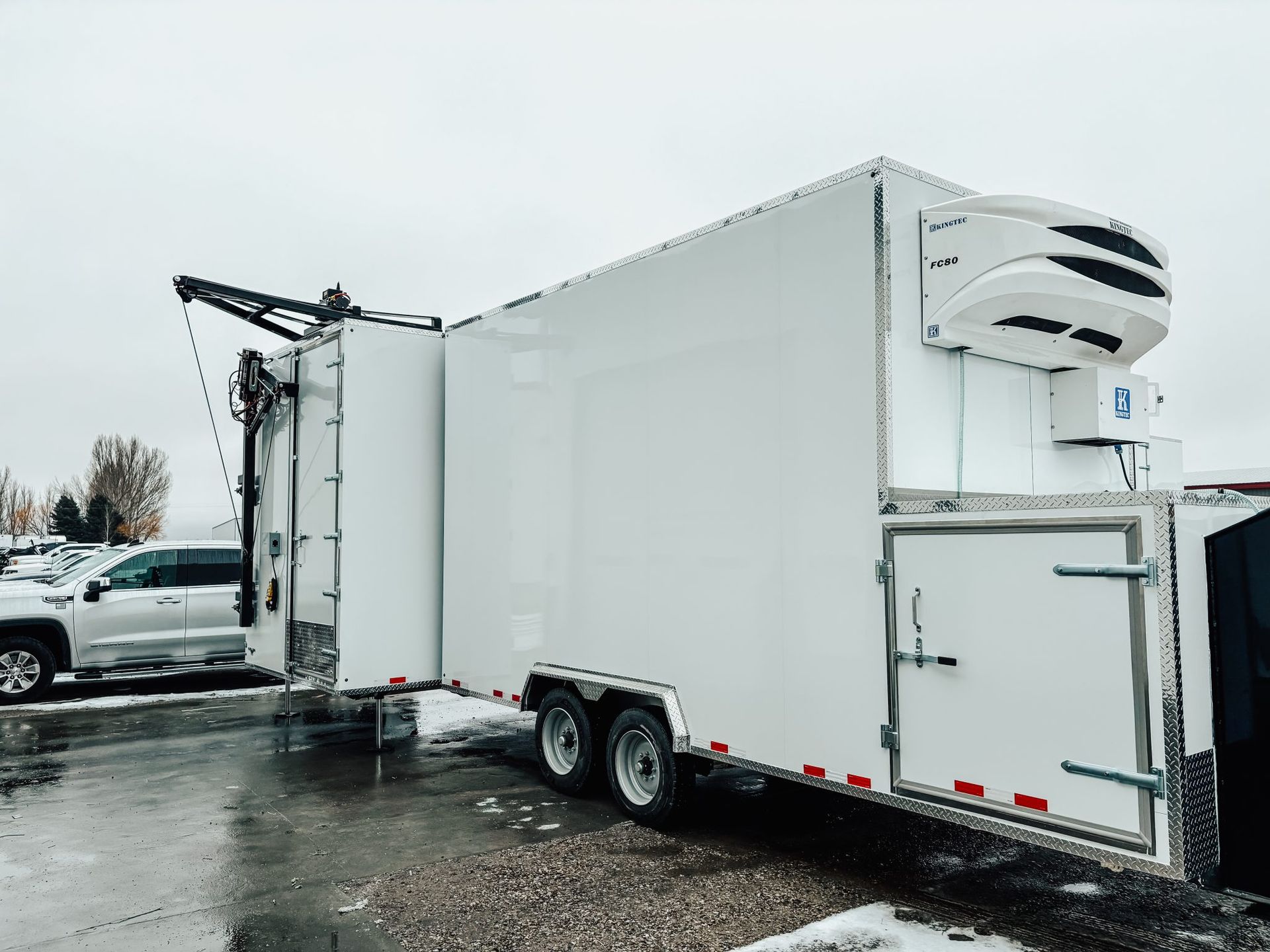 White refrigerated semi-trailer parked on wet pavement in a snowy lot