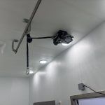 Ceiling-mounted  device with cables in a white hallway near a doorway.