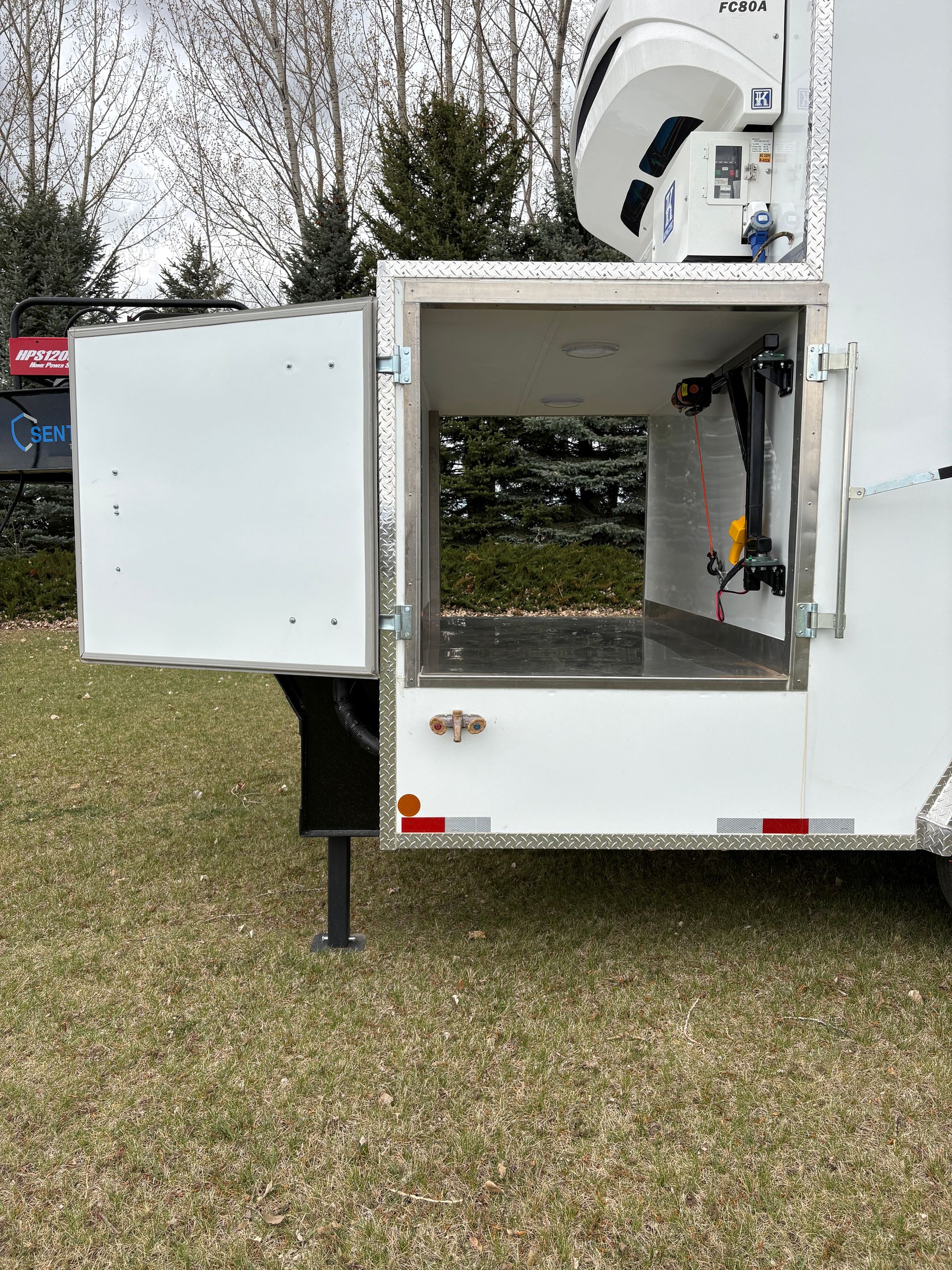 Open white utility trailer with side compartments and raised satellite dish on a grassy area