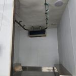 Empty narrow metal elevator interior with white walls and overhead lights inside meat processing trailer