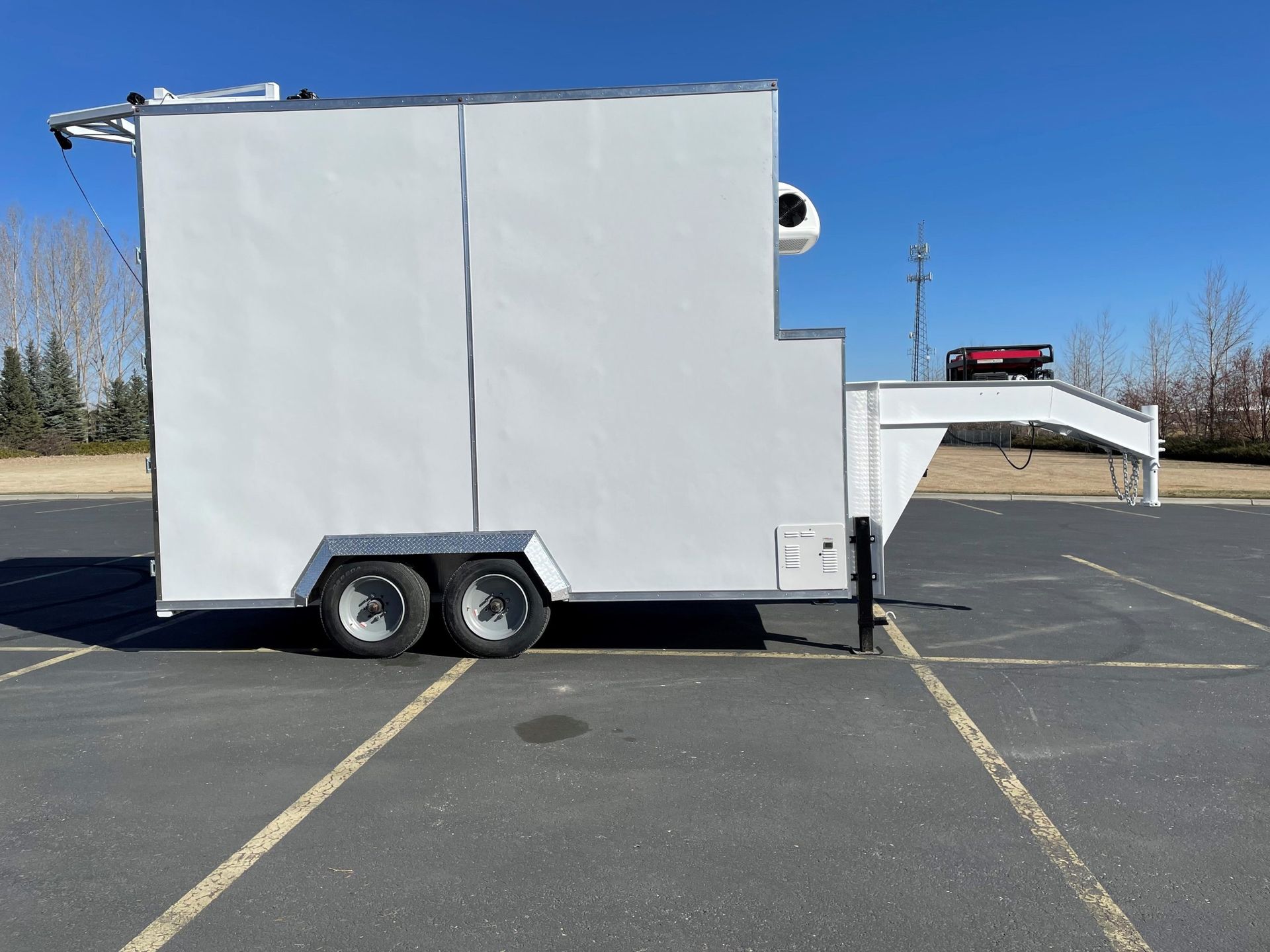 White box mobile meat processing trailer with a small front ramp parked in an empty parking lot under a blue sky
