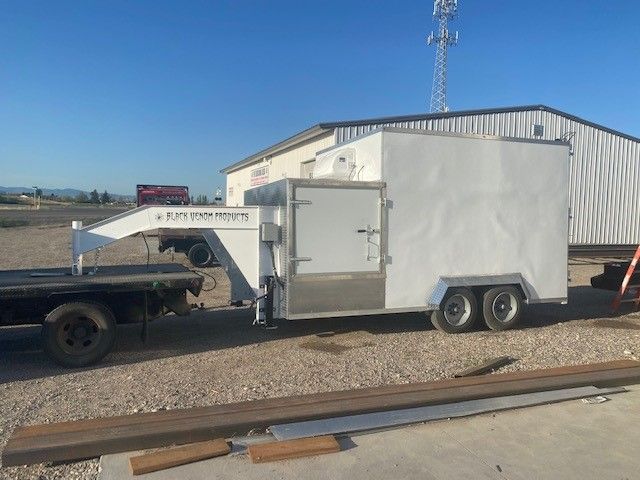 Meat processing trailer with front-mounted winch parked beside a warehouse on gravel
