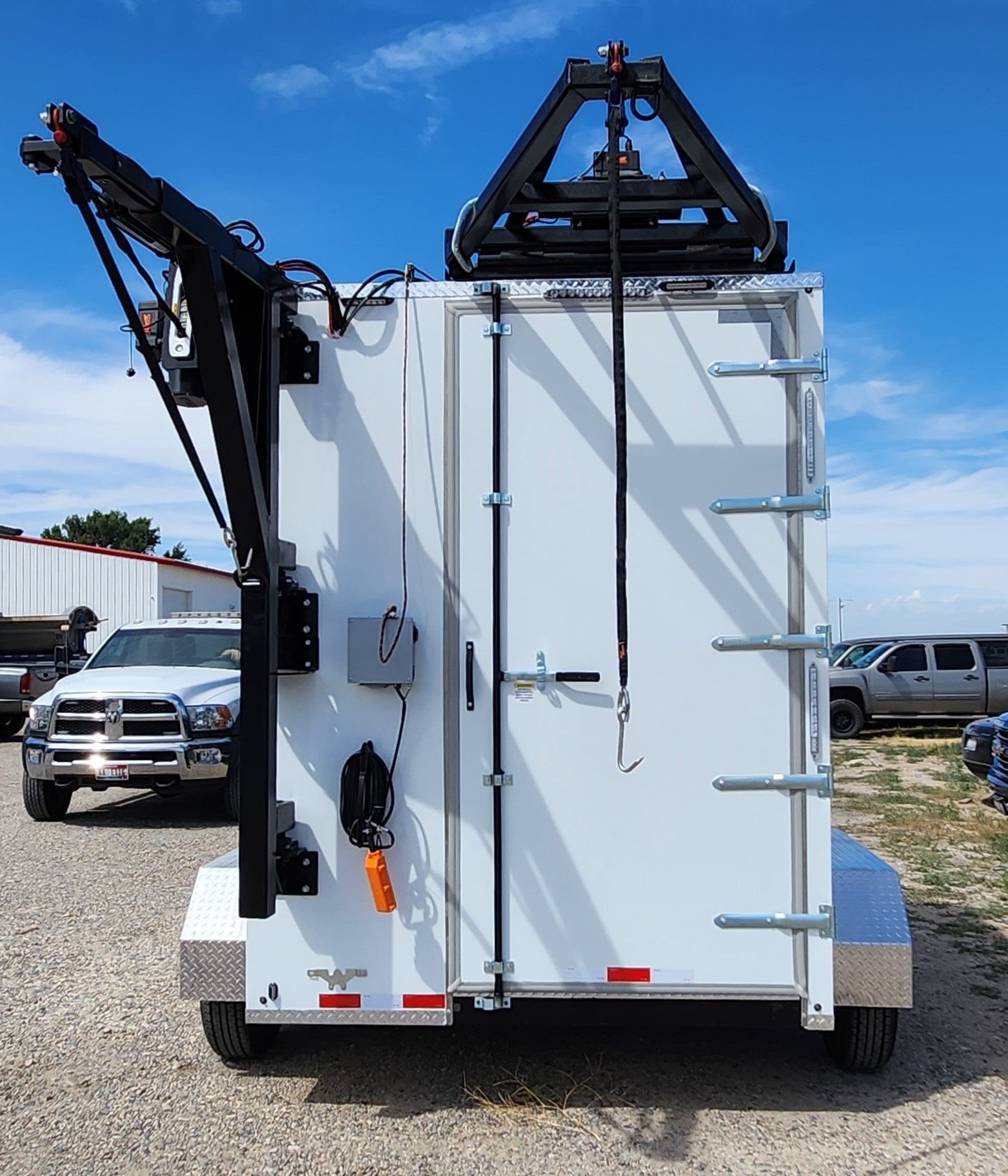 Rear view of a white slaughter trailer refrigerated trailer mounted crane equipment, parked outdoors under a blue sky