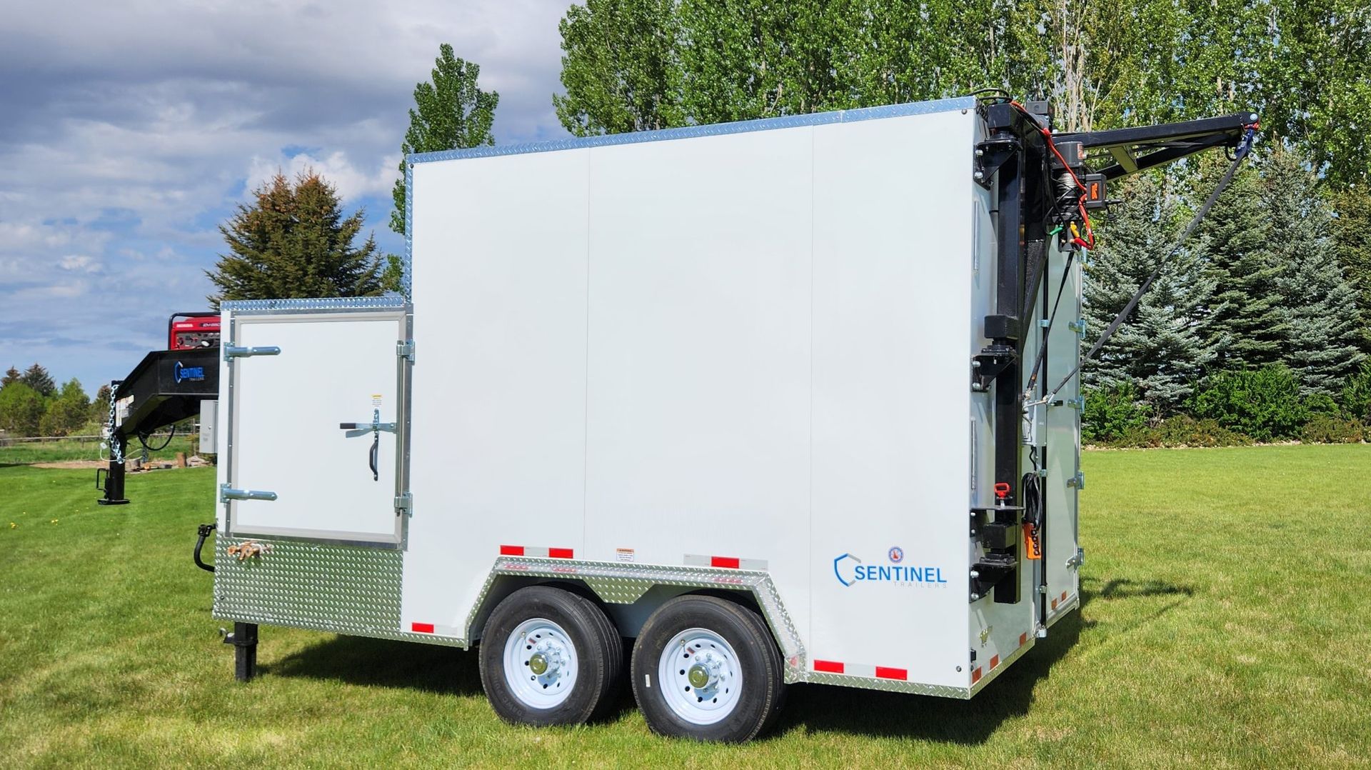 White enclosed utility trailer on grass with two axles, side door, and red reflectors outdoors under cloudy sky