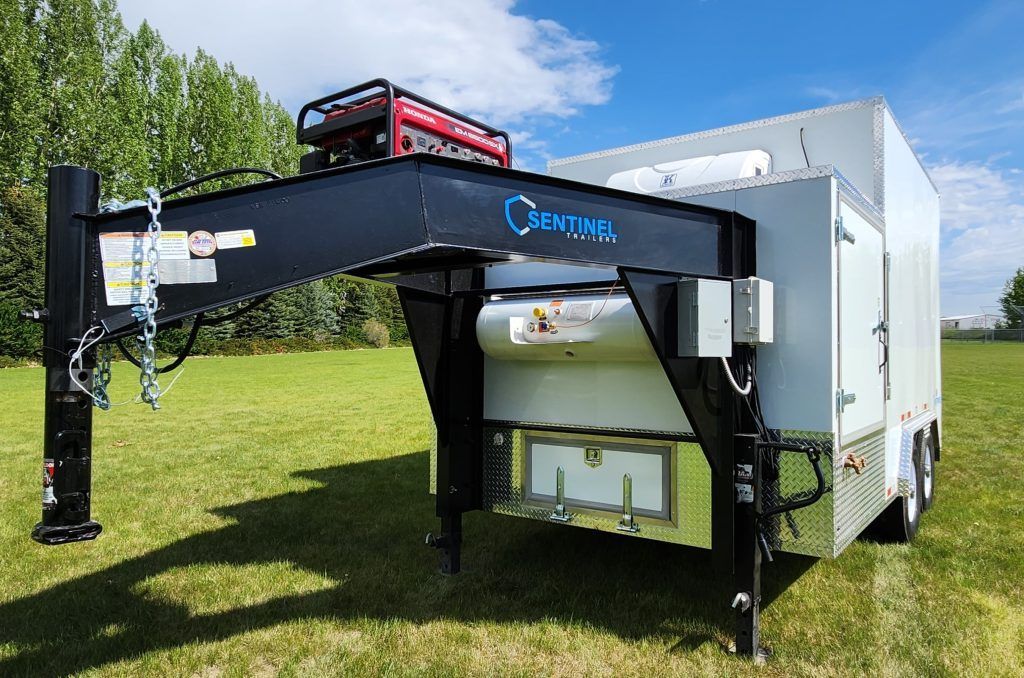 Black crane arm mounted on a white utility trailer by SEntinel trailers parked on grass under a blue sky