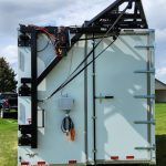White industrial trailer for meat processing with black support frame and equipment mounted on top, parked outdoors on grass.