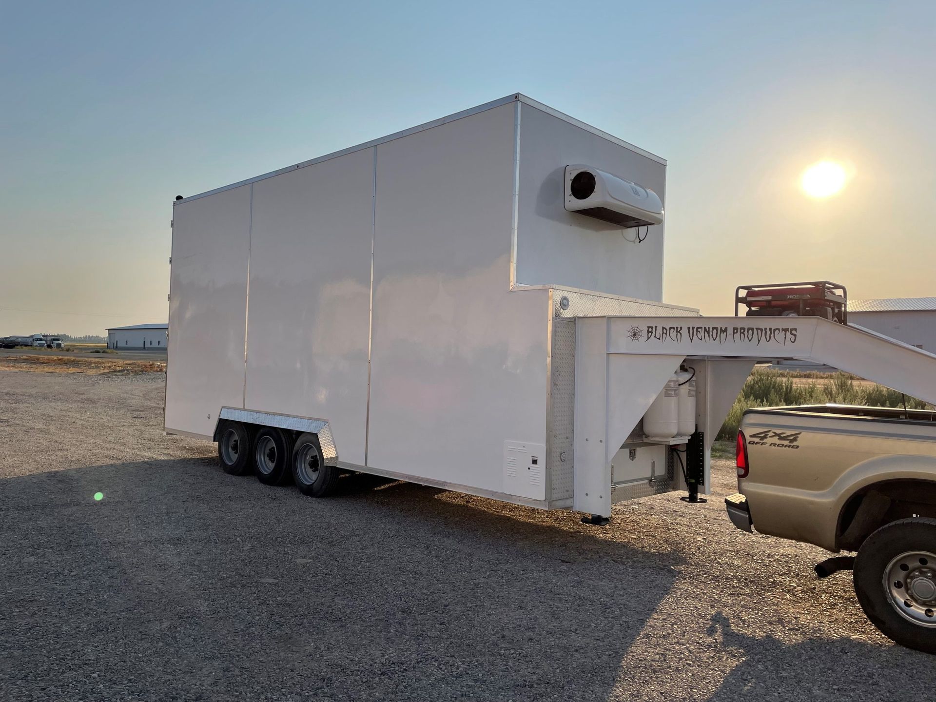 White Sentinel trailer-style unit on gravel at sunset, with a pickup truck beside a loading ramp.