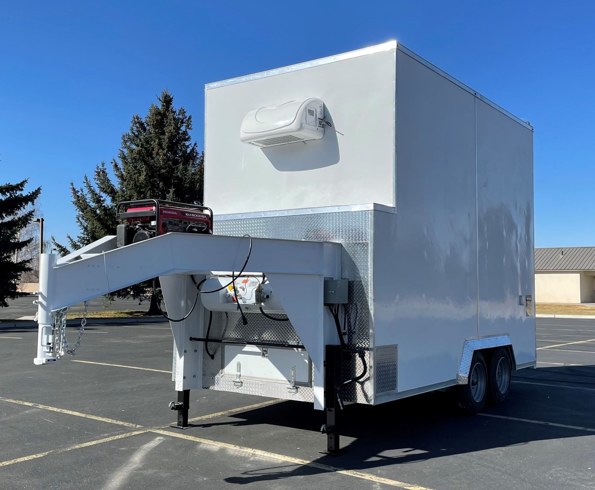 White slaughter trailer with a front-mounted car rack parked in an empty lot under a clear blue sky