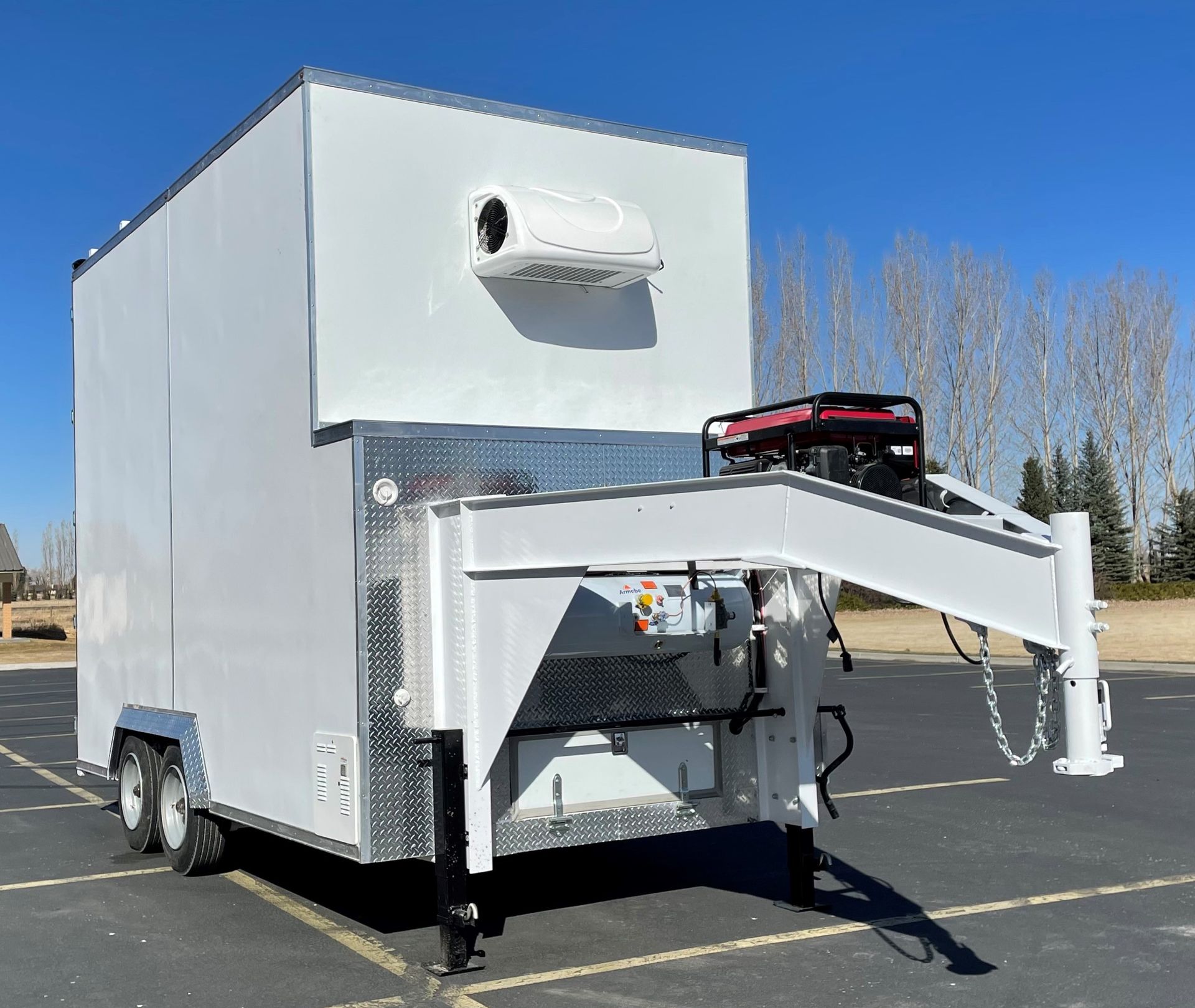 White enclosed processing trailer with a front hitch and generator parked outdoors on a sunny day