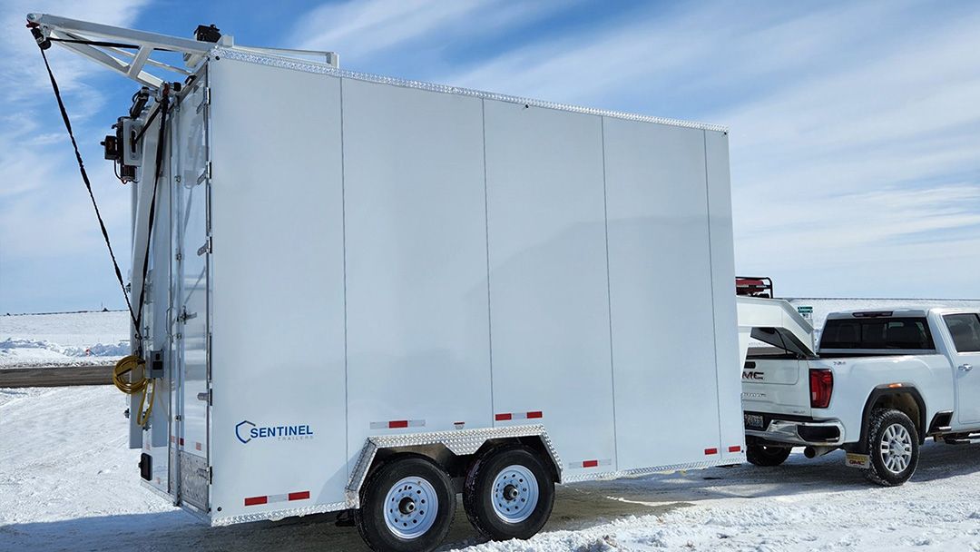 White enclosed trailer hitched to a pickup truck on a snowy roadside.