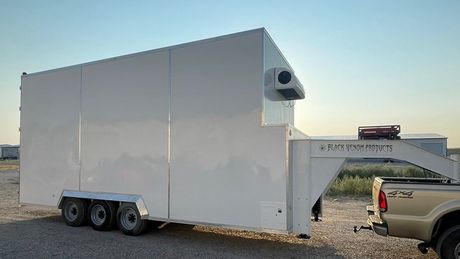 White enclosed refrigerated trailer hitched to a tan pickup in a parking lot at sunset
