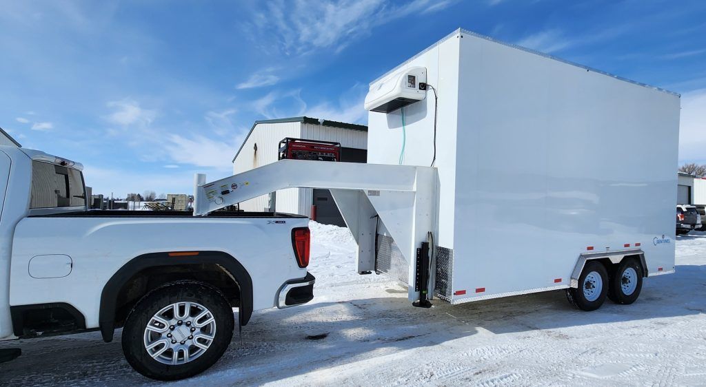 White pickup truck towing a white enclosed two-axle trailer in a snowy lot under a blue sky