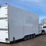 White box truck trailer parked outdoors on a gravel lot under a blue sky