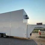 White box trailer parked on a gravel lot at sunset, with a side door, vents, and a small ramp on the right.