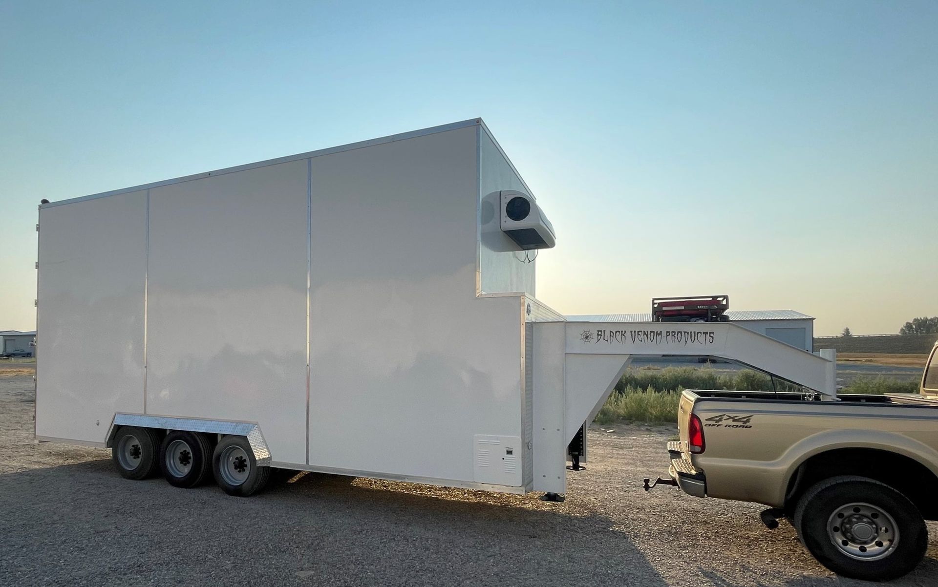 White enclosed Sentinel trailer with a raised front platform and vent, parked beside a pickup in an open lot.