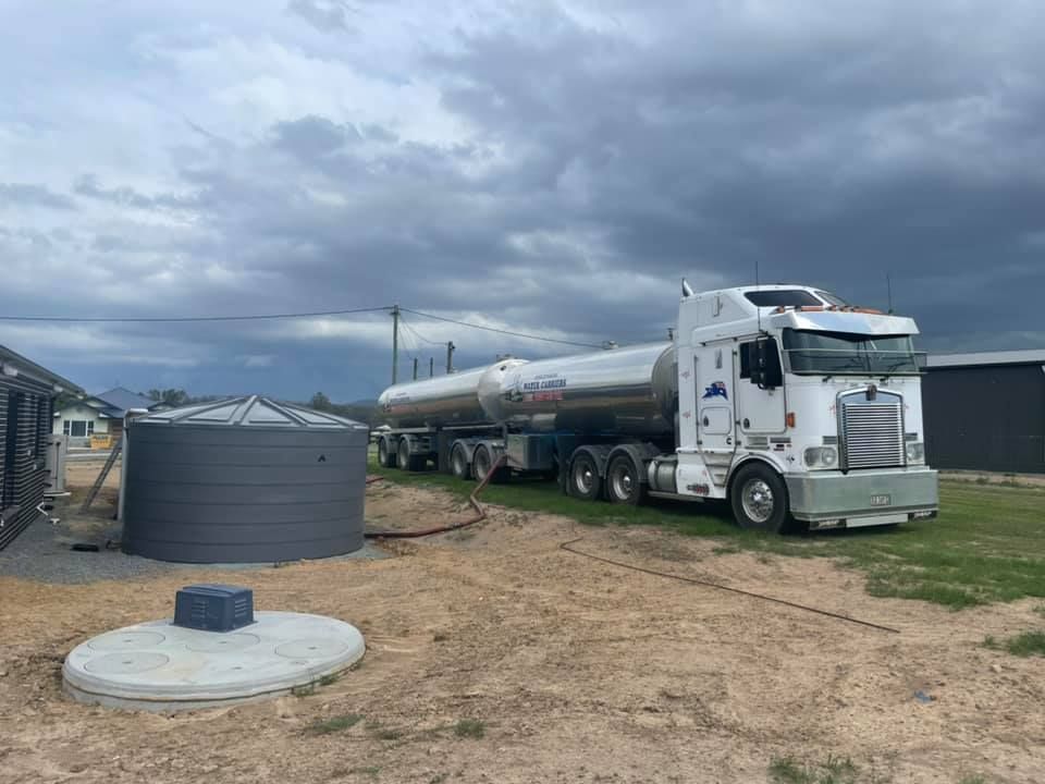 A White Semi Truck Is Parked in A Dirt Field Next to A Water Tank — Stolzenberg Water Carriers in Chatsworth, QLD